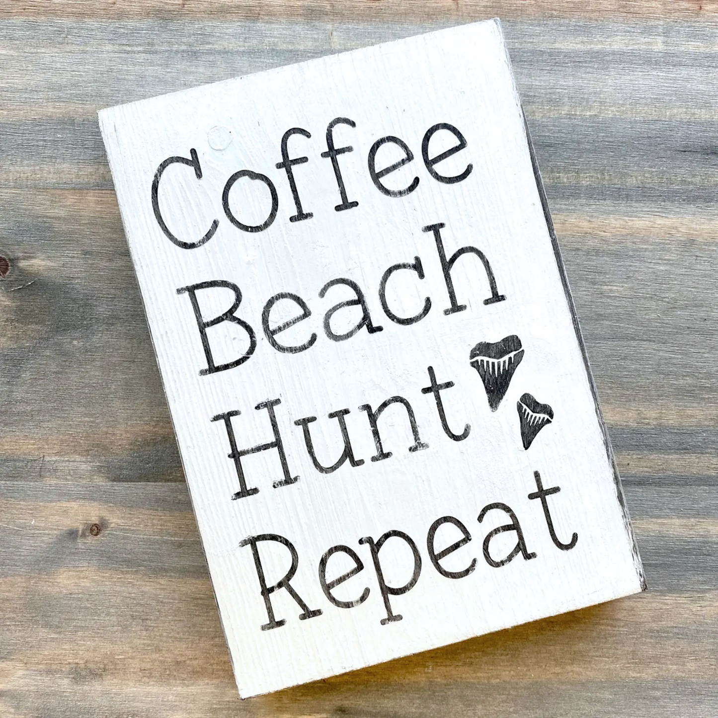 White sign with 'Coffee Beach Hunt Repeat' text on a wooden surface