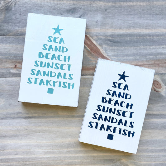 Two coastal Christmas signs with beachy text and starfish design on a wooden surface, Sea sand, beach sunset sandals and starfish in the shape of a christmas tree