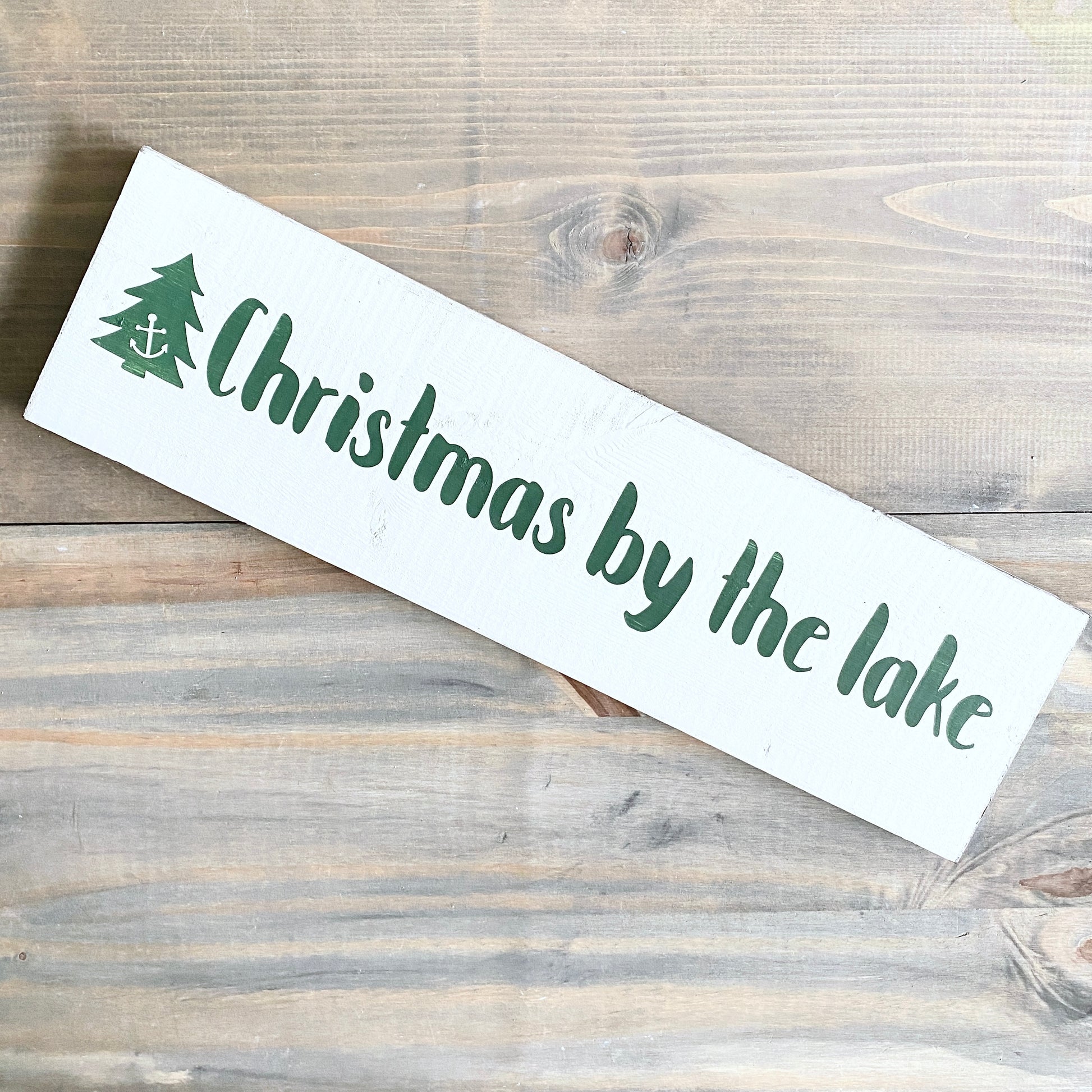 Wooden sign with 'Christmas by the lake' text and tree design on a wooden surface
