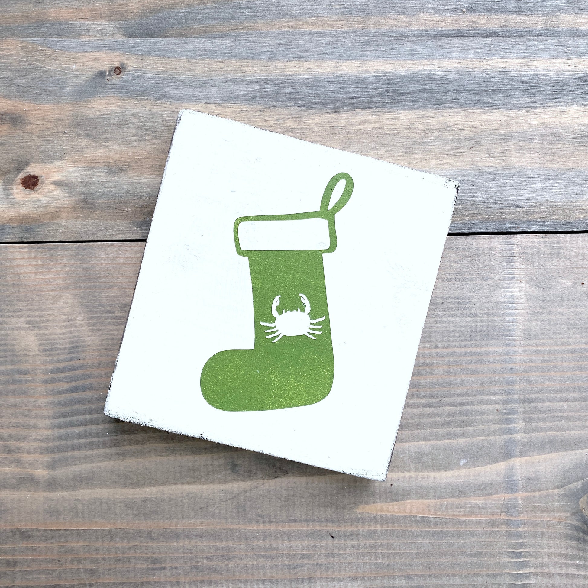 Green stocking with a white crab design on a white card, placed on a wooden surface.
