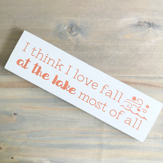 Wooden sign with text 'I think I love fall at the lake most of all' on a wooden surface