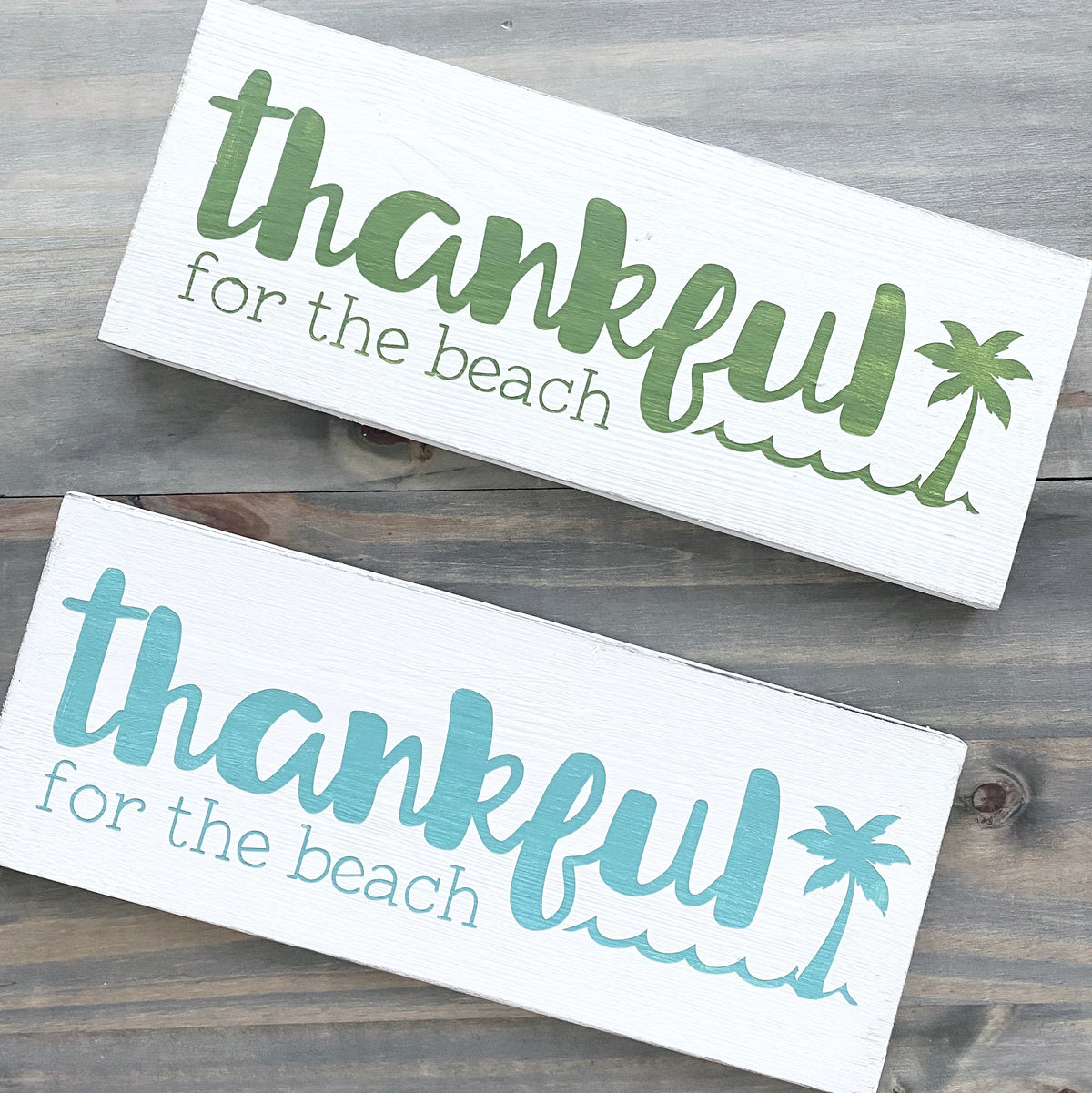two white signs on a wood background with text- thankful for the each and a palm tree and wave, one in green, one in aqua