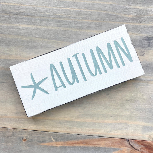 Wooden sign with 'AUTUMN' and a starfish on a wooden surface