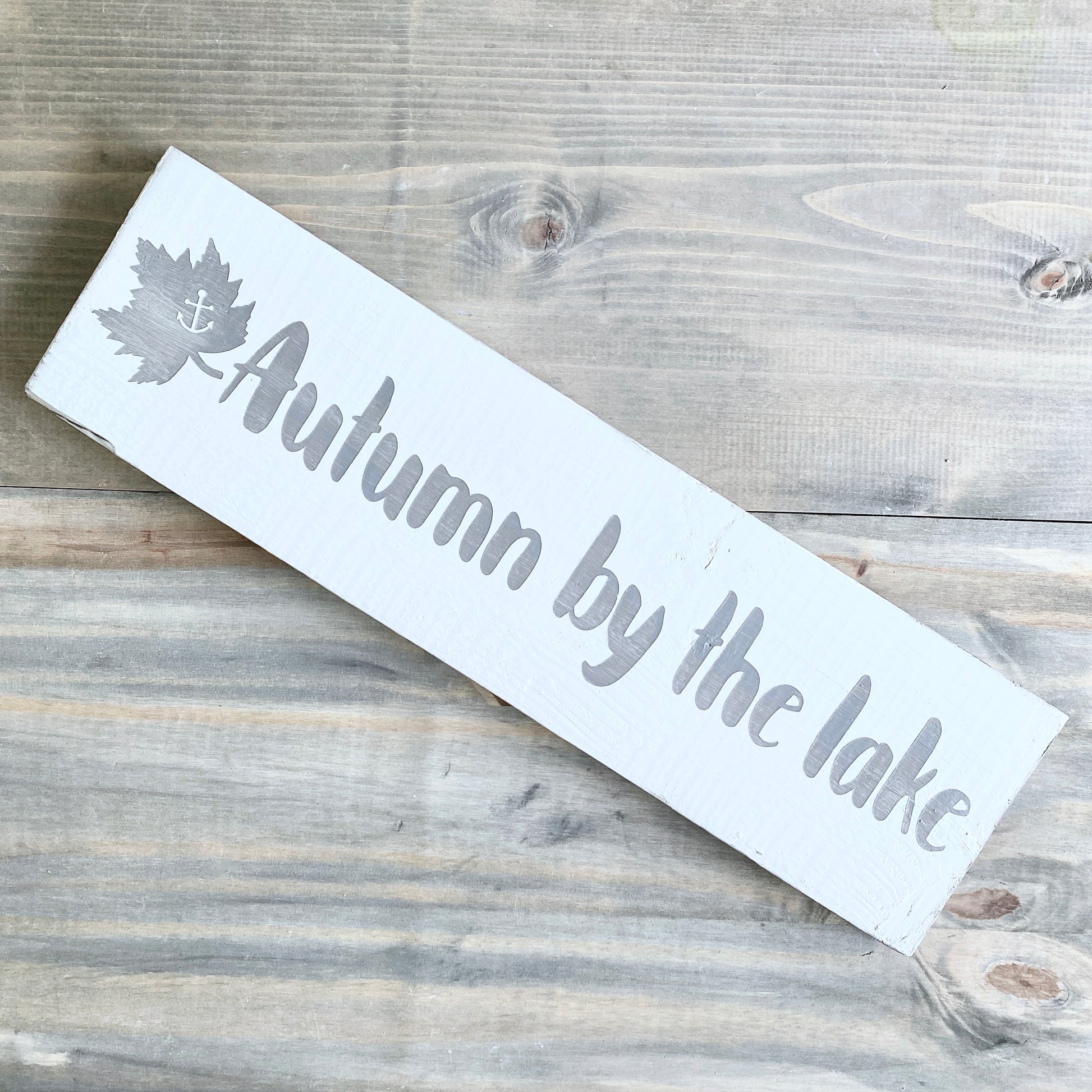 White sign with 'Autumn by the lake' text and leaf design on a wooden surface