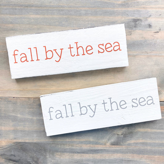 Two signs with 'fall by the sea' text on a wooden surface