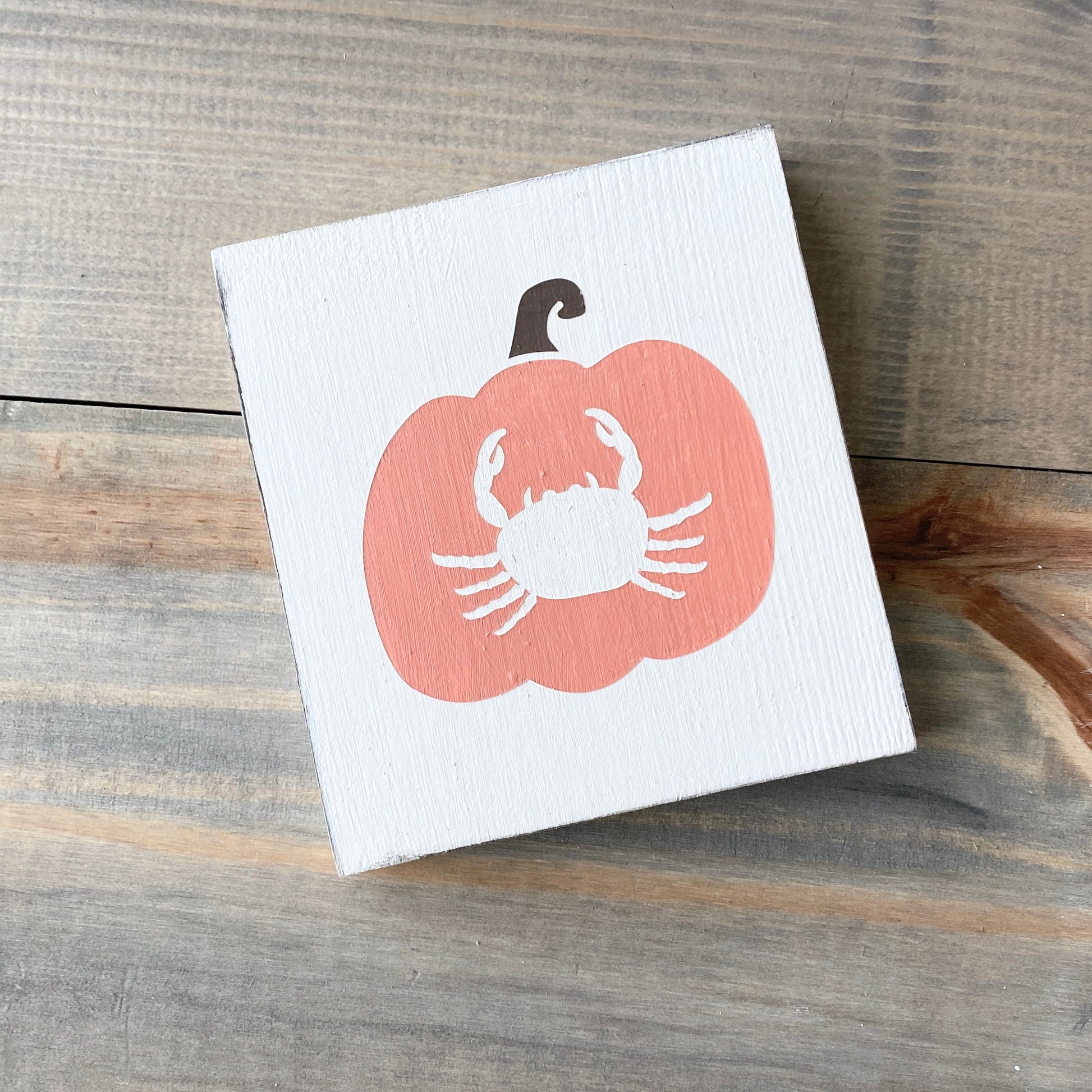 Small white board with a orange pumpkin design featuring a white crab on a wooden surface