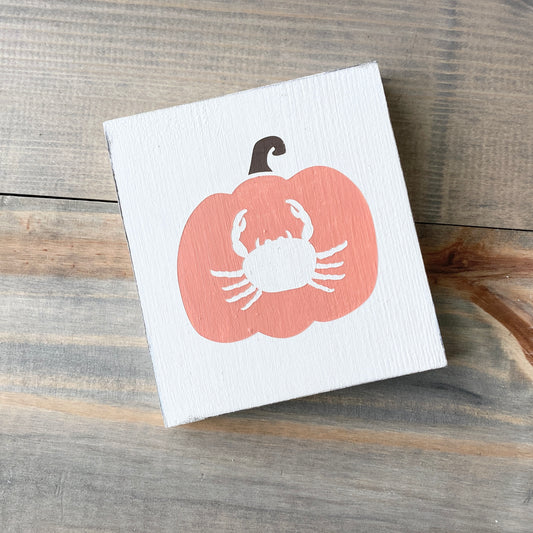 Small white board with a orange pumpkin design featuring a white crab on a wooden surface