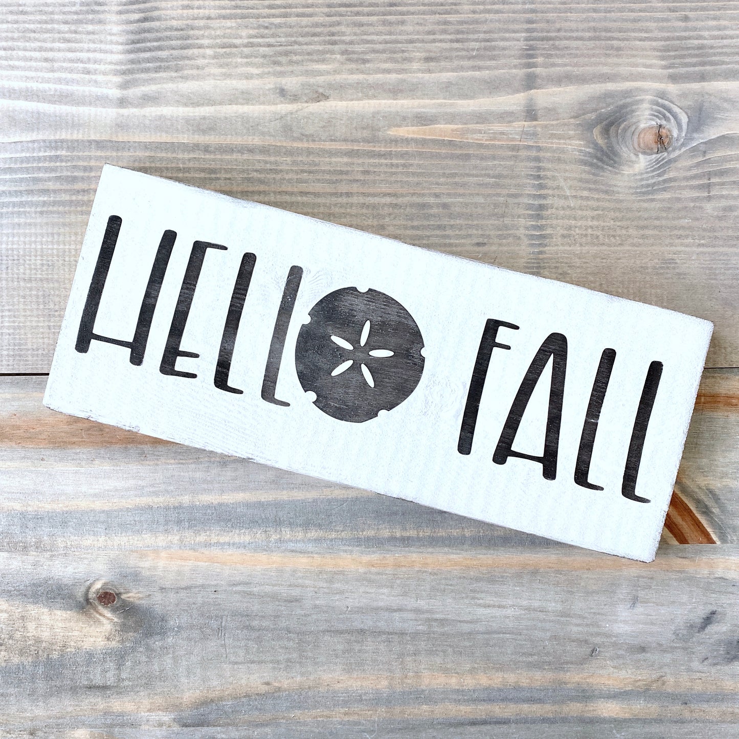 White sign with 'Hello Fall' text on a wooden surface