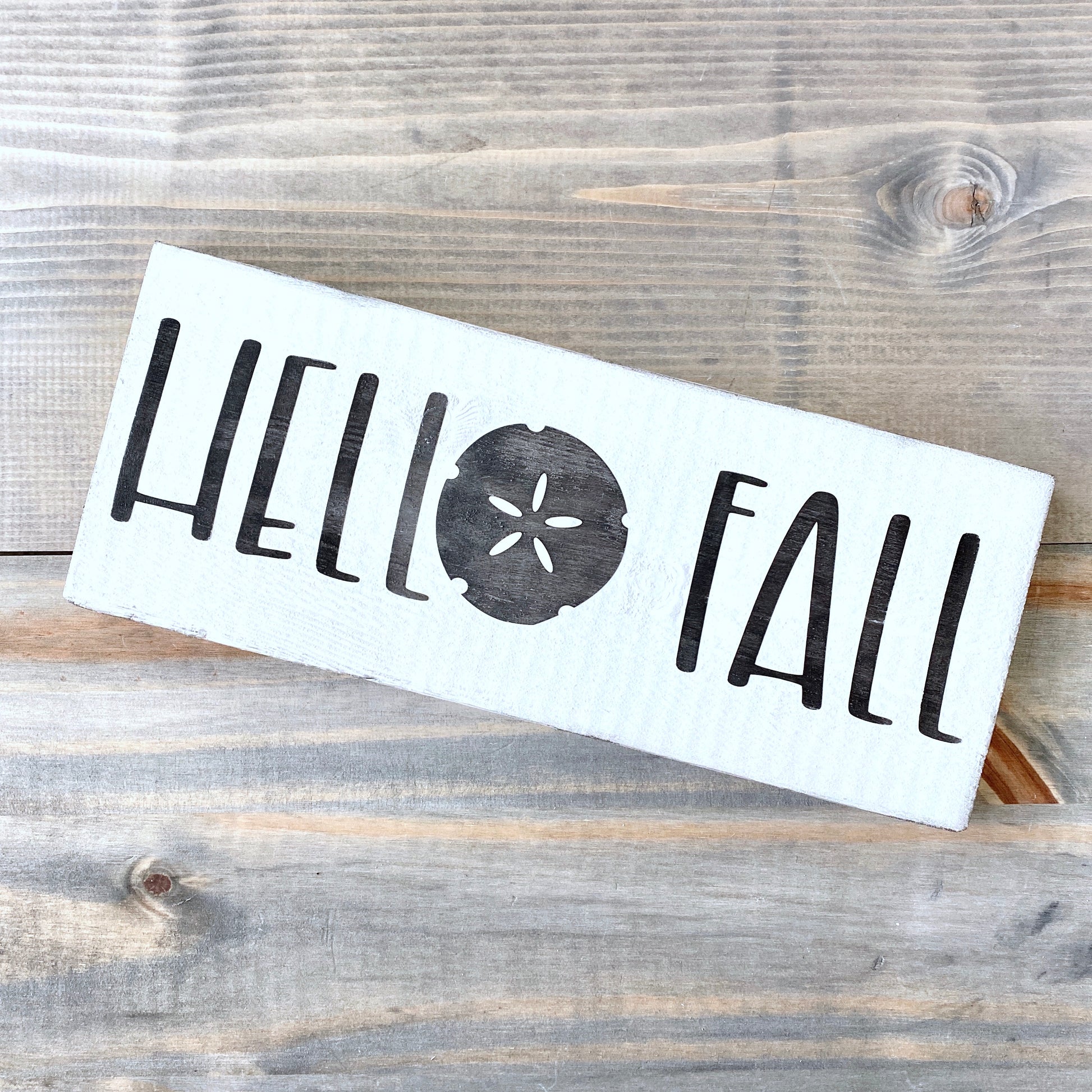 White sign with 'Hello Fall' text on a wooden surface