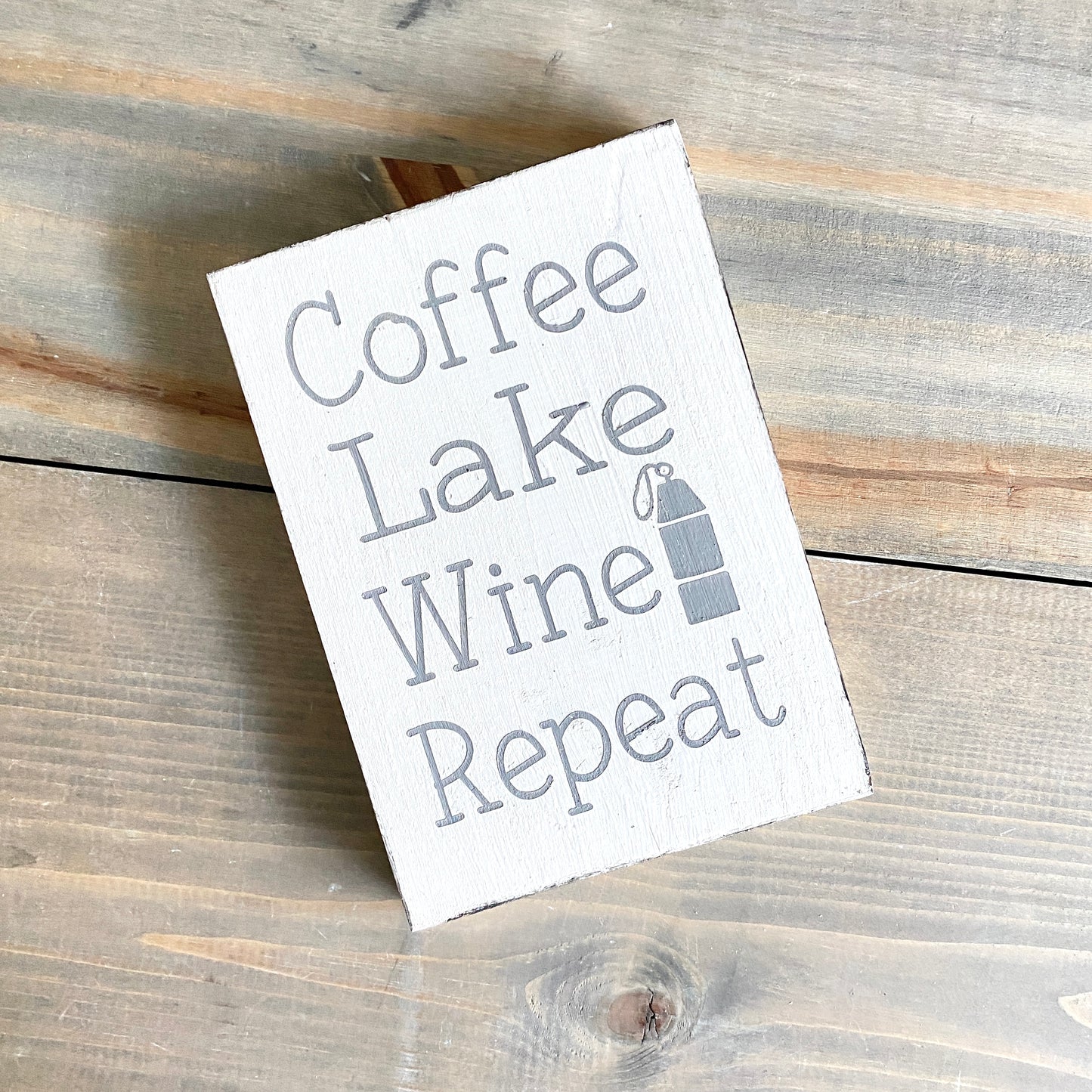 Wooden sign with 'Coffee Lake Wine Repeat' text on a wooden surface