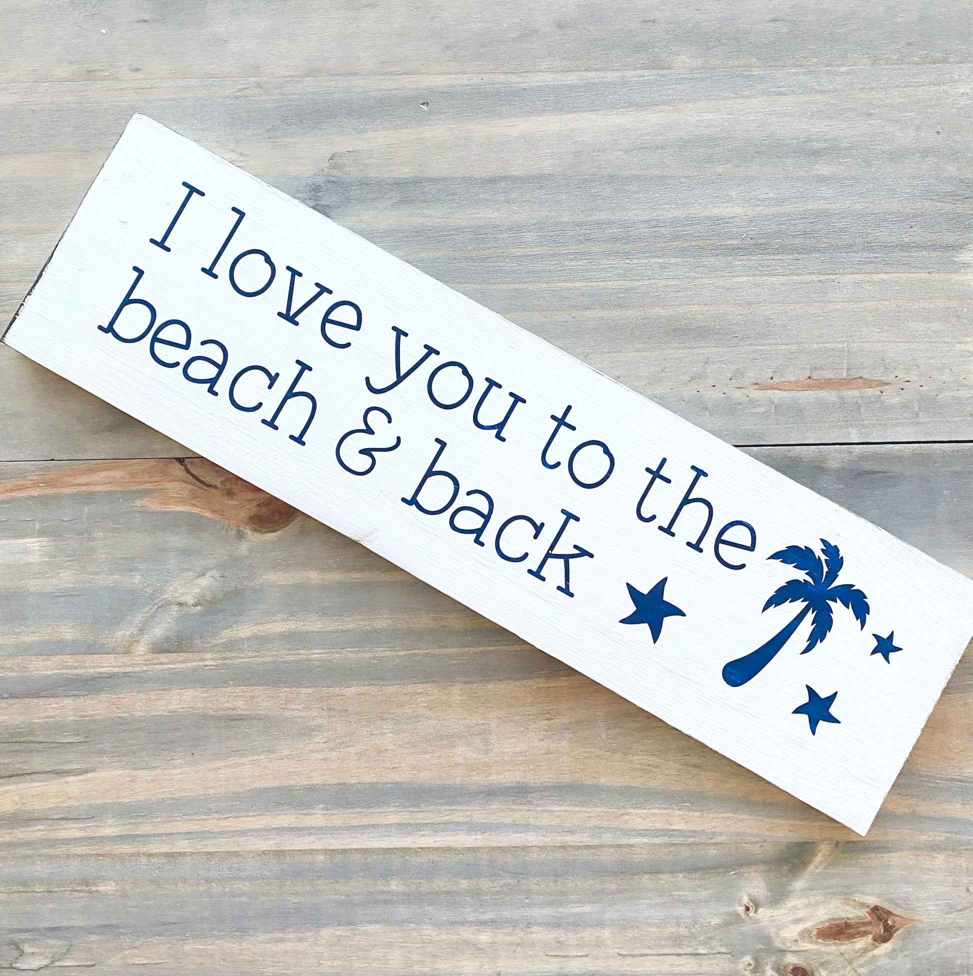 Wooden sign with 'I love you to the beach & back' text and palm tree design on a wooden surface.