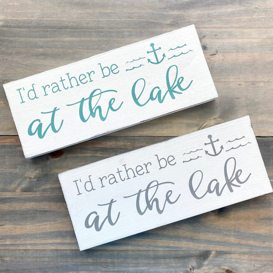 Two wooden signs with 'I'd rather be at the lake' text on a wooden surface. Nautical lake decor
