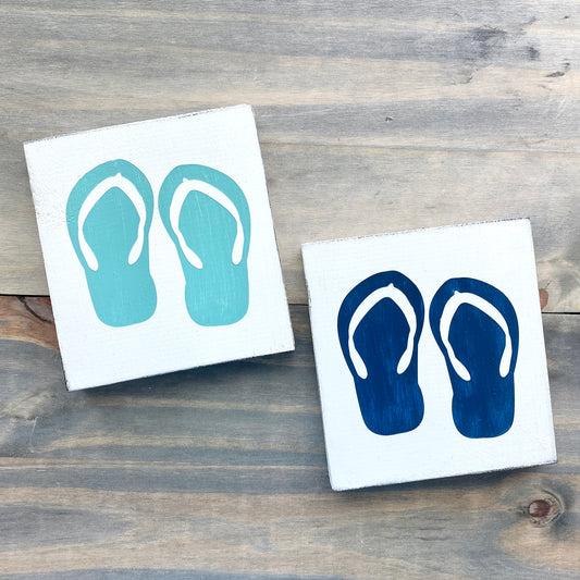 Two square signs with flip-flop designs on a wooden surface
