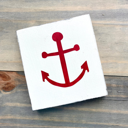 White square sign with a red anchor on a wooden surface