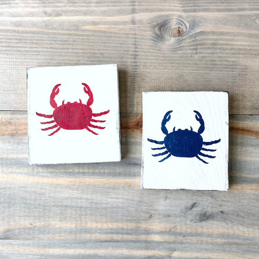 Two wooden signs with crab designs on a wooden surface