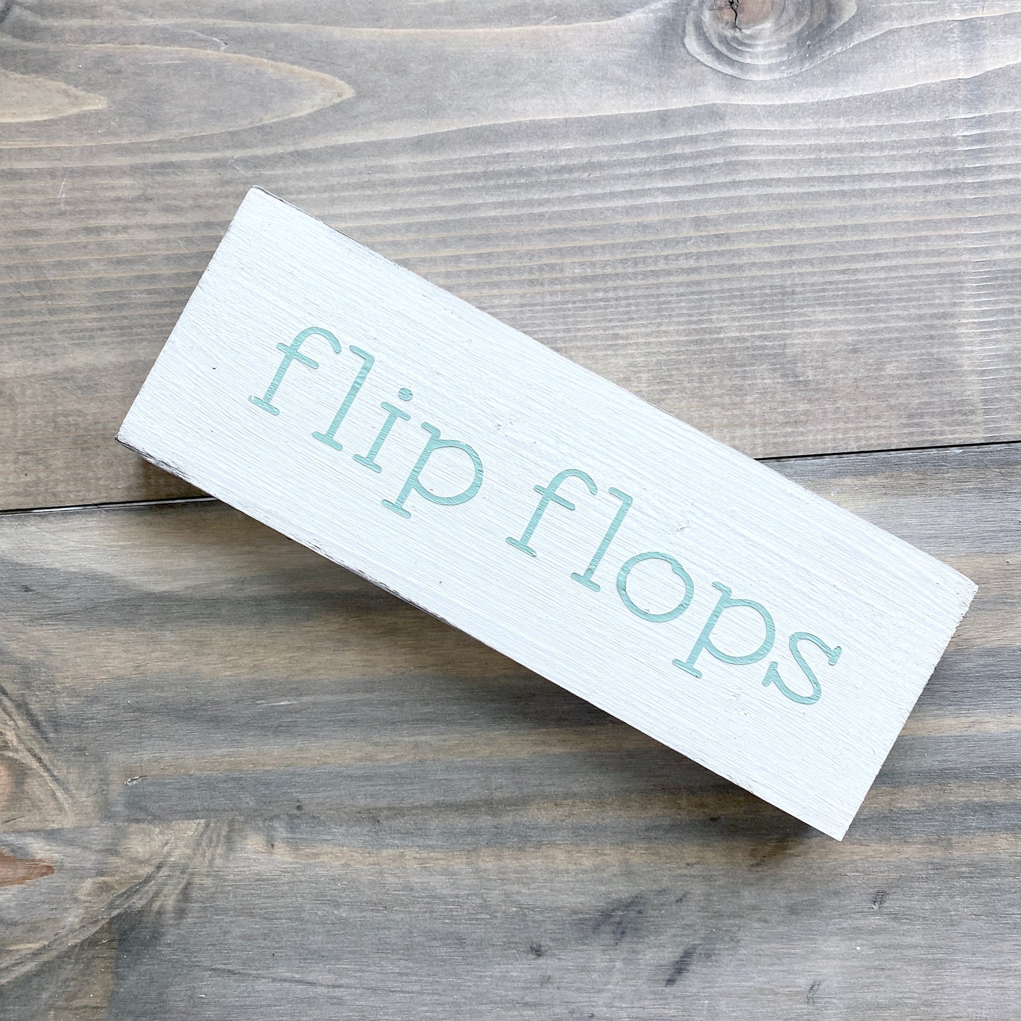 White rectangular sign with 'flip flops' text on a wooden surface