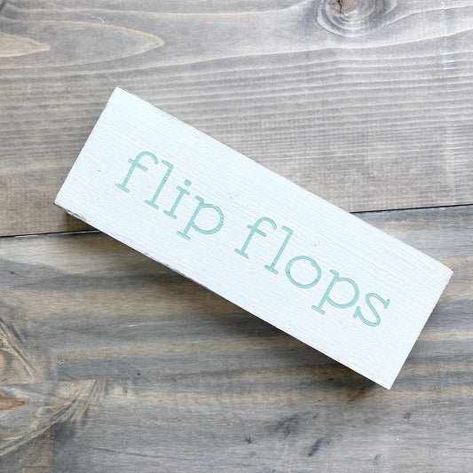 White rectangular sign with 'flip flops' text on a wooden surface