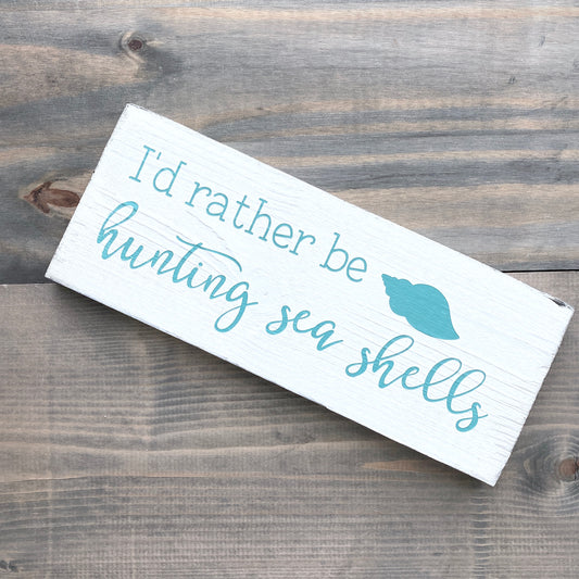 Wooden sign with text 'I'd rather be hunting sea shells' on a wooden surface