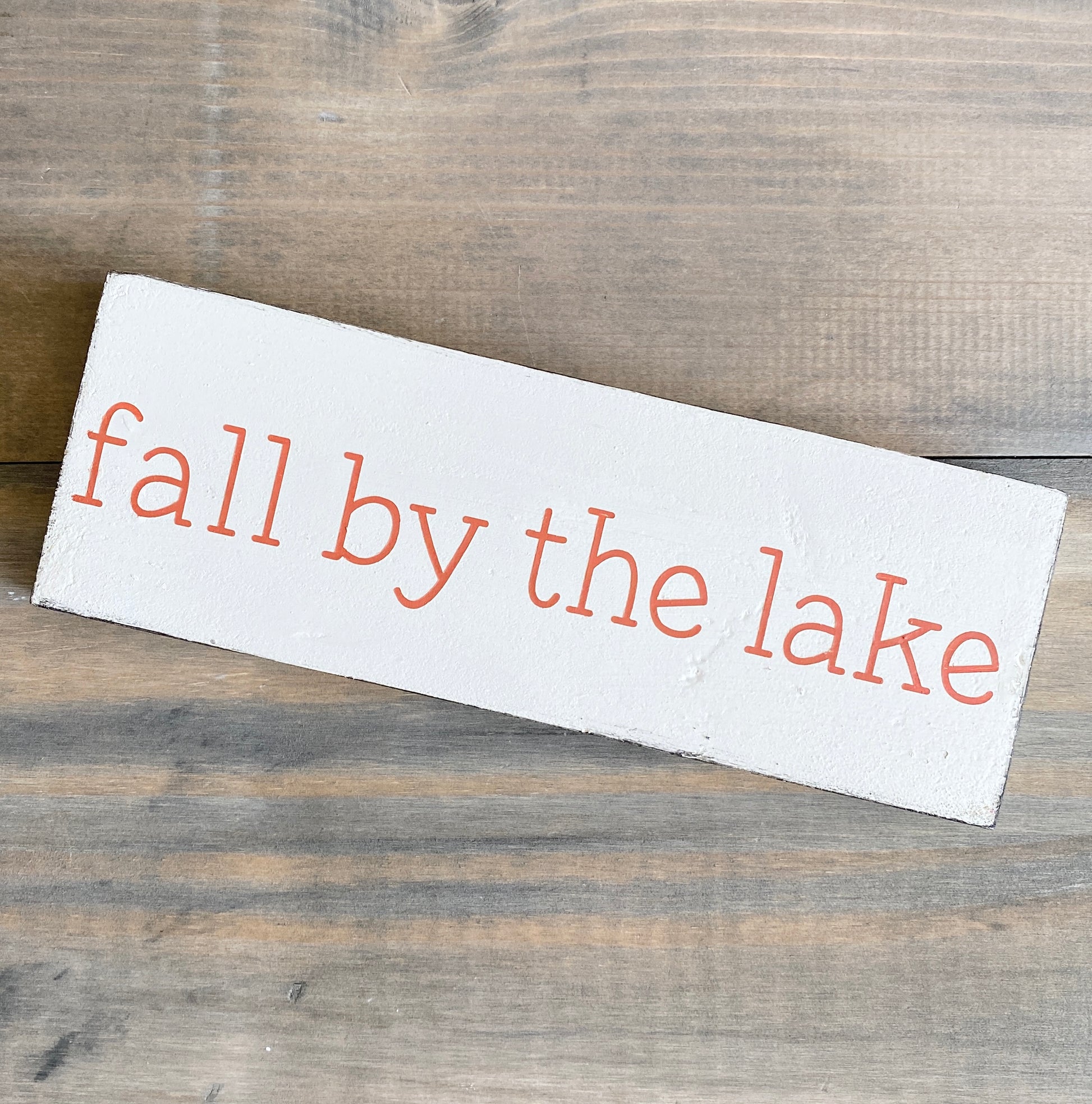 Wooden sign with 'fall by the lake' text on a wooden surface