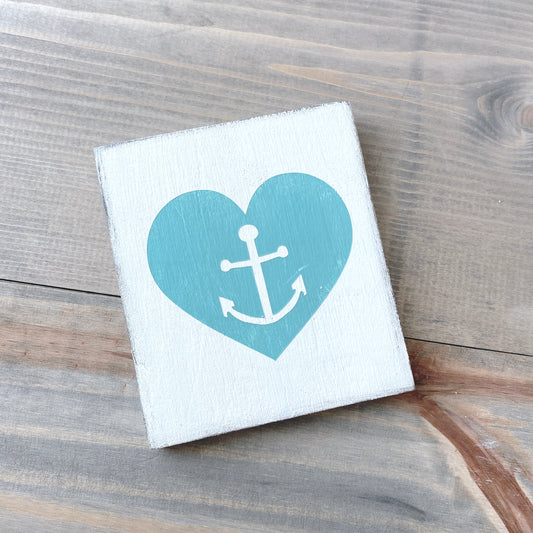 Small white sign with an aqua heart and white anchor on a wooden surface