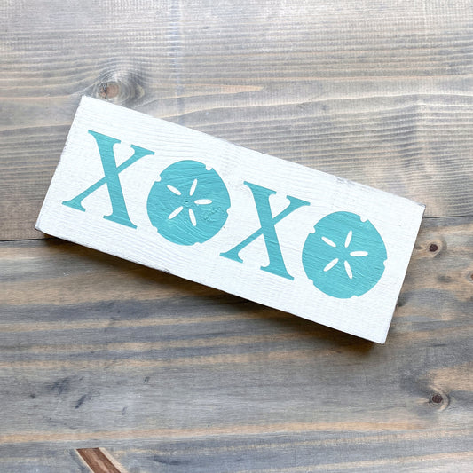 Wooden sign with 'XOXO' and sand dollar designs on a wooden surface