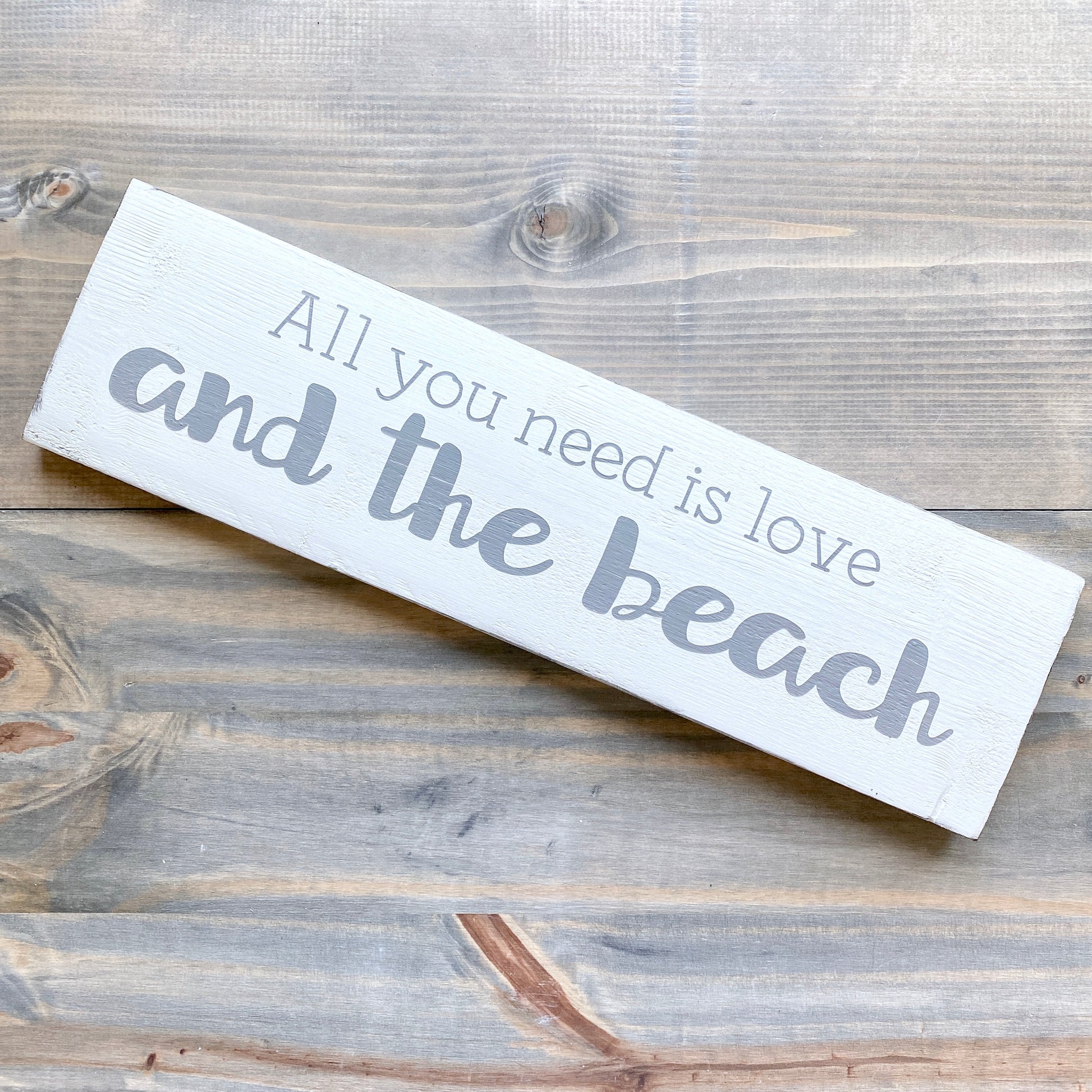 Wooden sign with 'All you need is love and the beach' text on a wooden surface