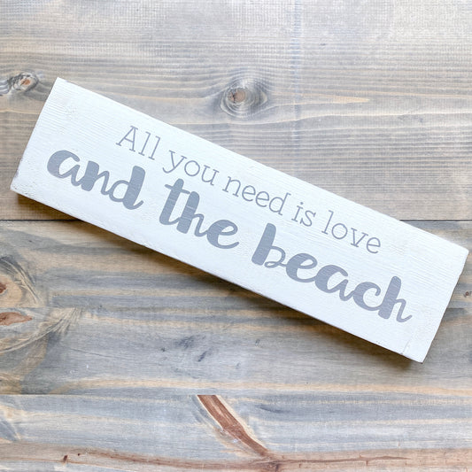 Wooden sign with 'All you need is love and the beach' text on a wooden surface