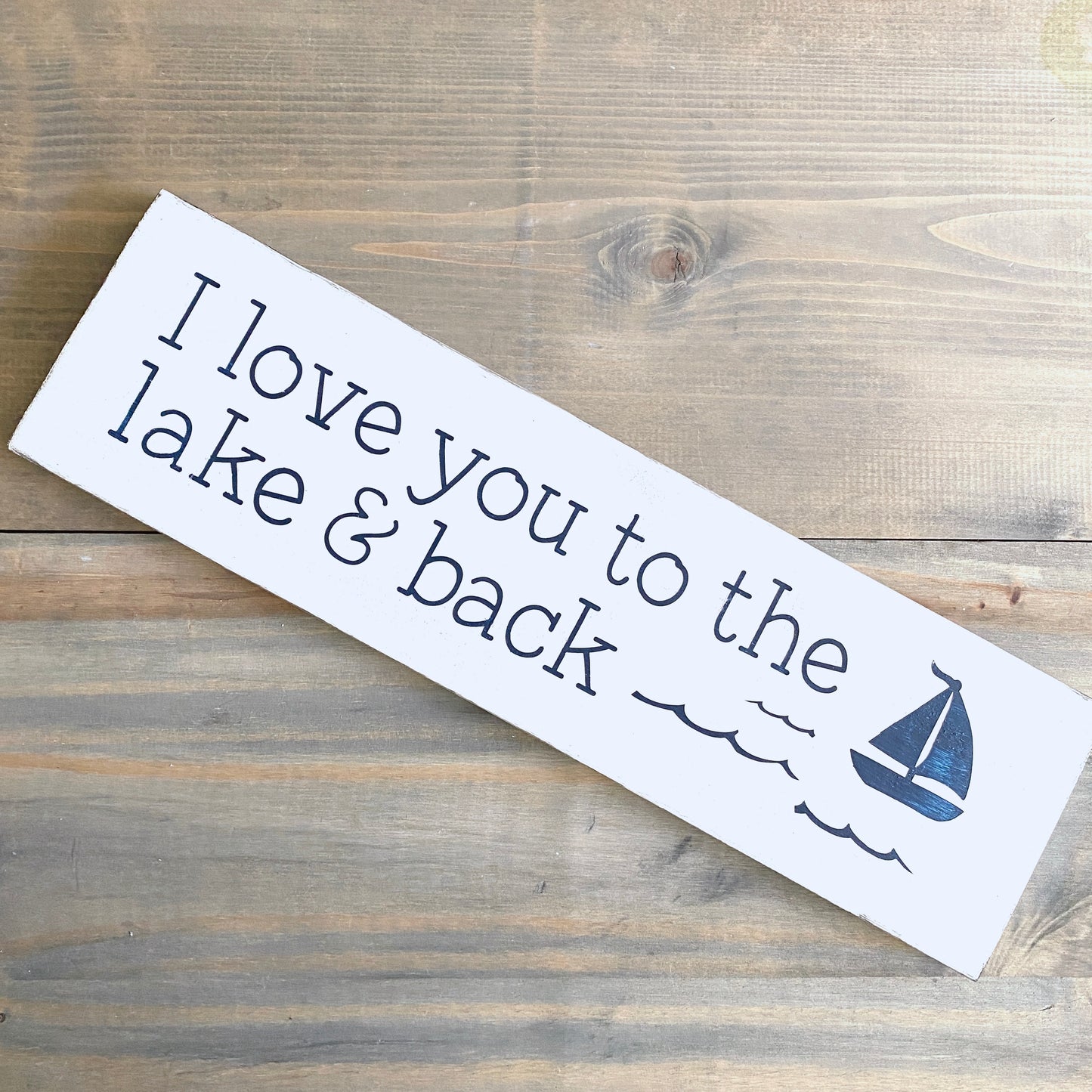 Wooden sign with 'I love you to the lake & back' text and a sailboat on a wooden surface