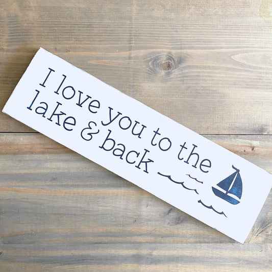 Wooden sign with 'I love you to the lake & back' text and a sailboat on a wooden surface