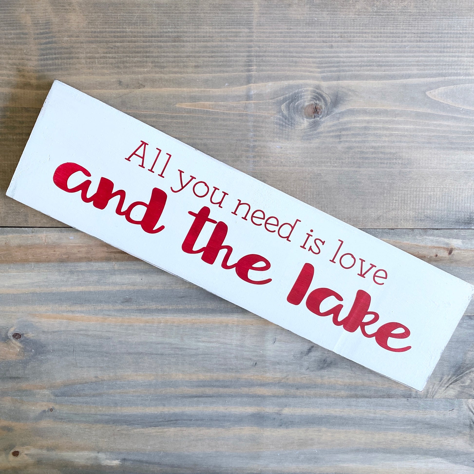 Wooden sign with 'All you need is love and the lake' text on a wooden surface