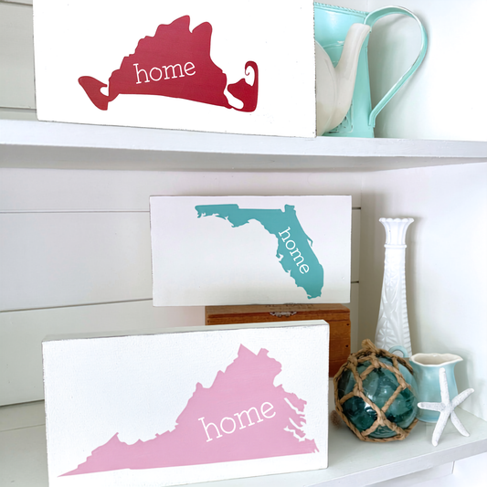 Decorative signs of states with 'home' text on a shelf with decorative items.