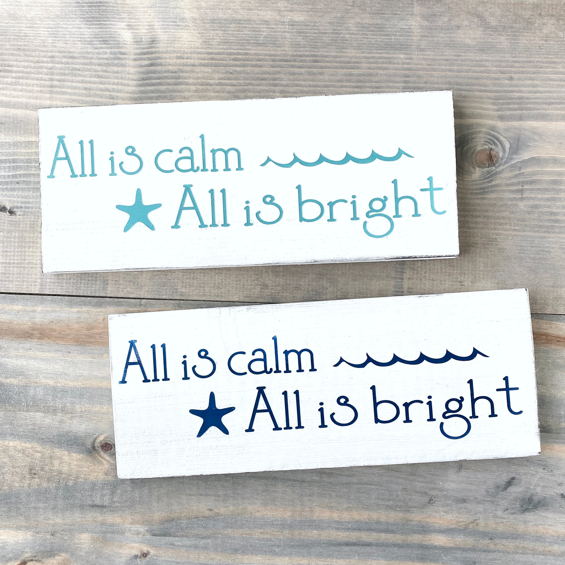 Two rectangular signs with text and a starfish on a wooden background All is calm, all is bright, coastal christmas sign
