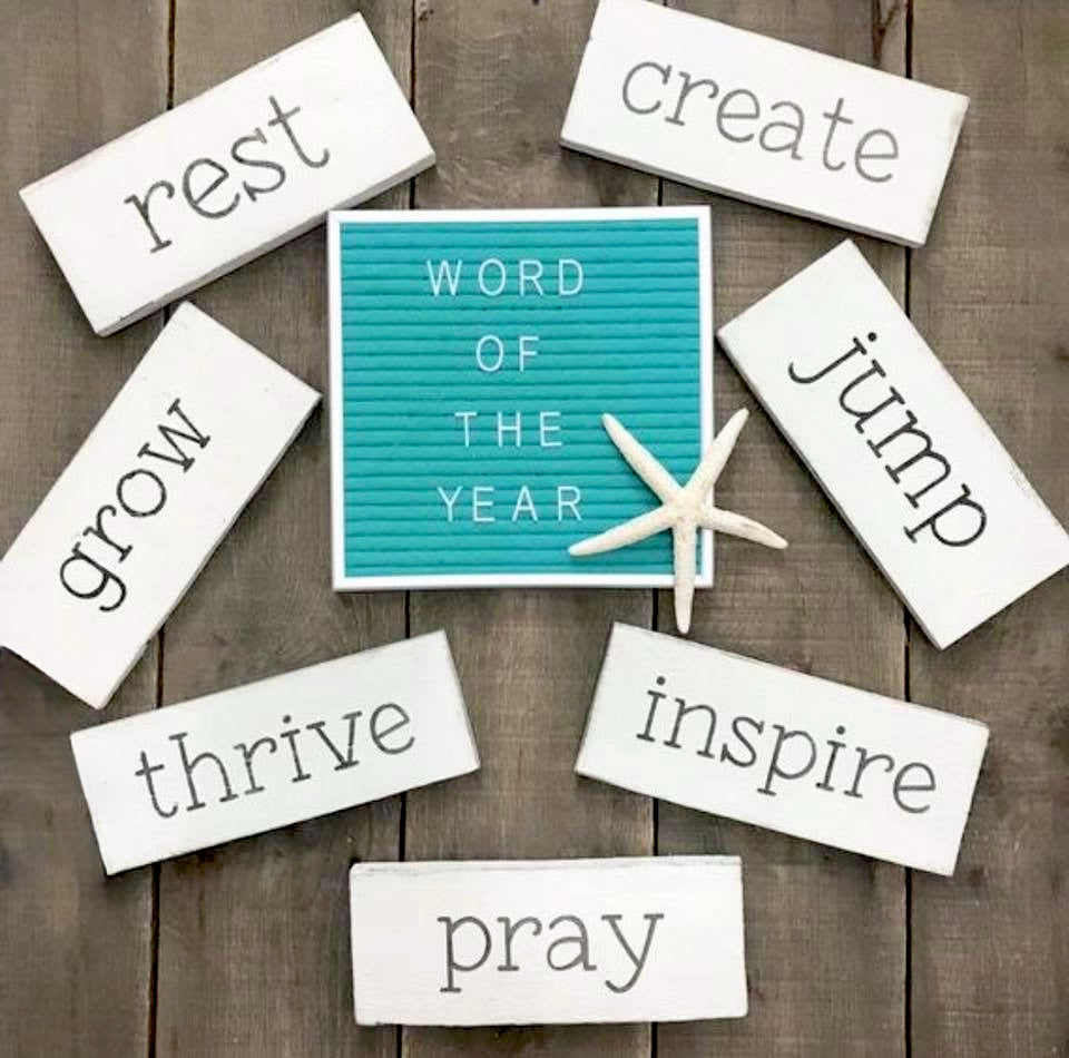 Motivational word signs on a wooden surface with a central turquoise sign displaying 'WORD OF THE YEAR'.